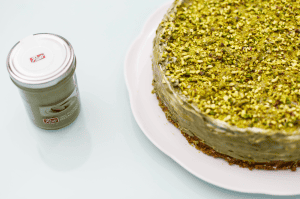 Pistachio cake topped with crushed pistachios and a pistachio cream jar beside it.