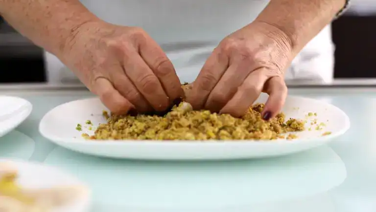 Handmade Sicilian pistachio filling preparation. Hand pressing pistachio filling on a white plate.