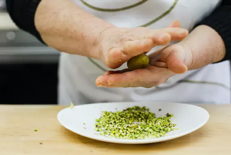 Pistì artisanal Sicilian sweets preparation Hand rolling pistachio paste with chopped pistachios on a white plate.