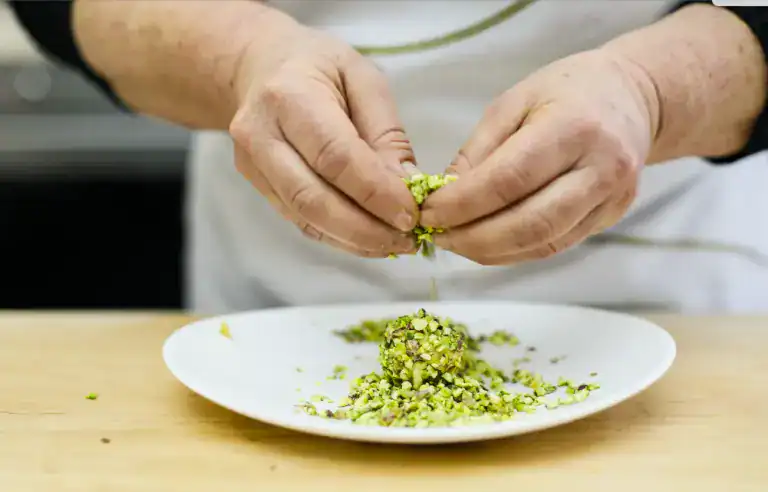 Pistì Pistachio Processing Hands crushing pistachios on a white plate for artisanal Sicilian sweets.