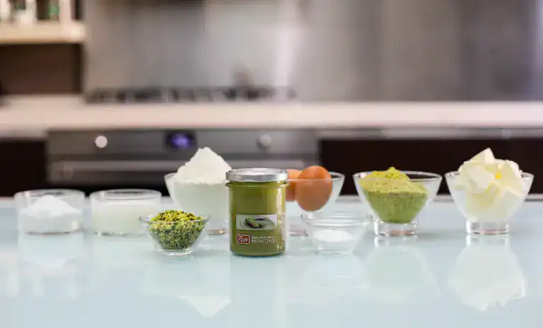 Pure Sicilian Pistachio Paste Artisanal pistachio paste jars and ingredients on a kitchen counter.