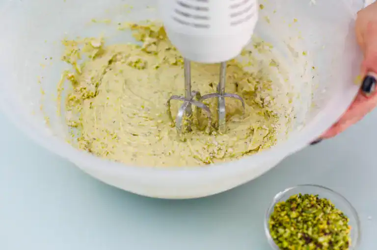 Creamy pistachio filling preparation Mixing pistachio filling with an electric hand mixer in a white bowl.