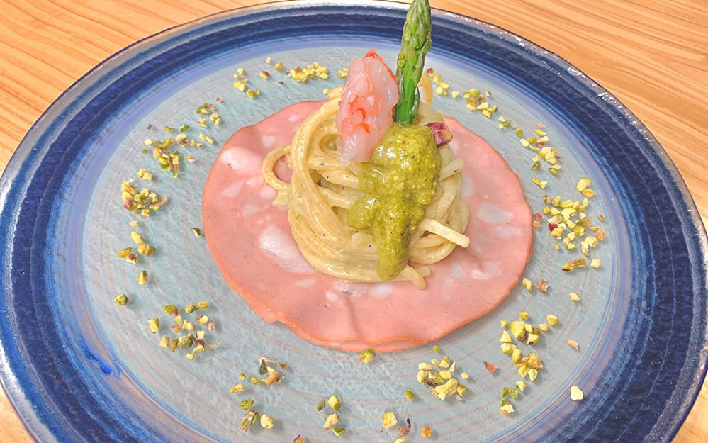 Pasta with pink sauce, asparagus, and green pesto, garnished with crushed pistachios.
