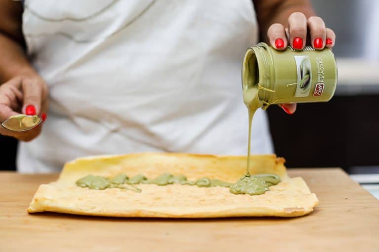 Pomodoro verde su pasta sfoglia Person pouring green sauce onto pastry dough, Sicilian culinary scene.