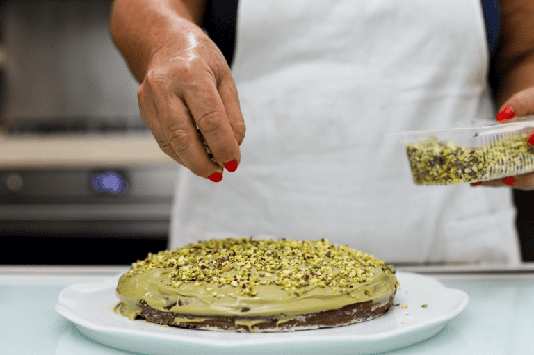 Pistì artisanal Sicilian cake Woman decorating a Sicilian cake with pistachios and green toppings.