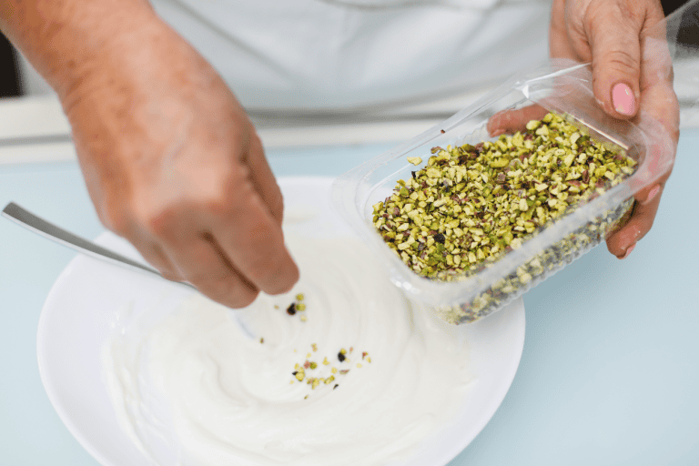 Pistì Pistachio Topping Freshly chopped pistachios being added to creamy dessert.
