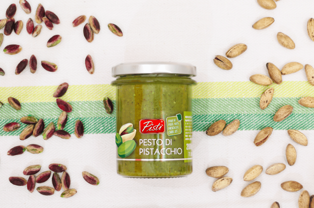Jar of Sicilian pistachio pesto with scattered pistachios around it.
