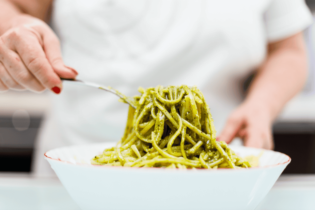 Pasta al pesto con basilico e pinoli, servita in una ciotola bianca.