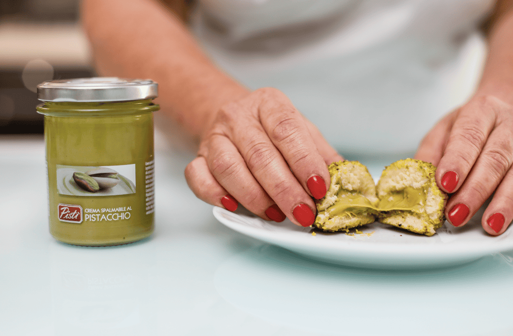 Artisanal pistachio cream jar with a person holding a pistachio pastry.