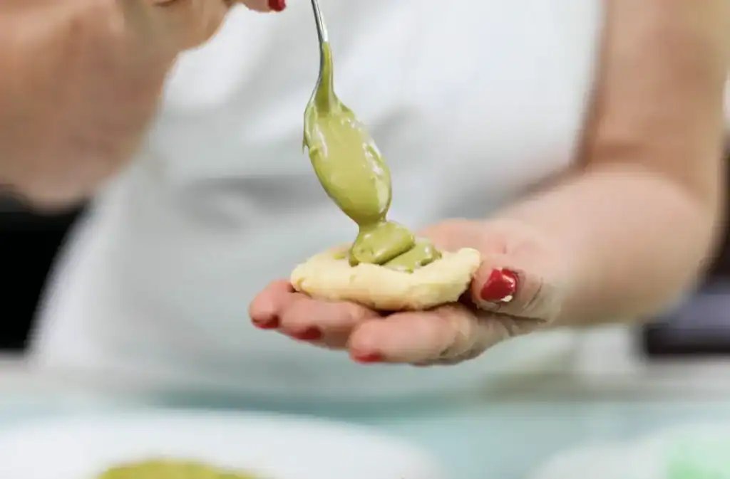 Pistì artisanal Sicilian sweets being prepared Close-up of green pistachio cream being spooned onto a cookie.