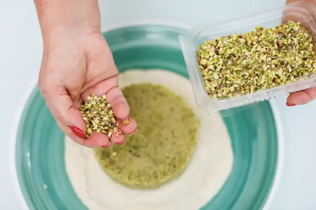 Pistì Pistachio Filling Preparation Hand adding chopped pistachios into dough for Sicilian pastry.