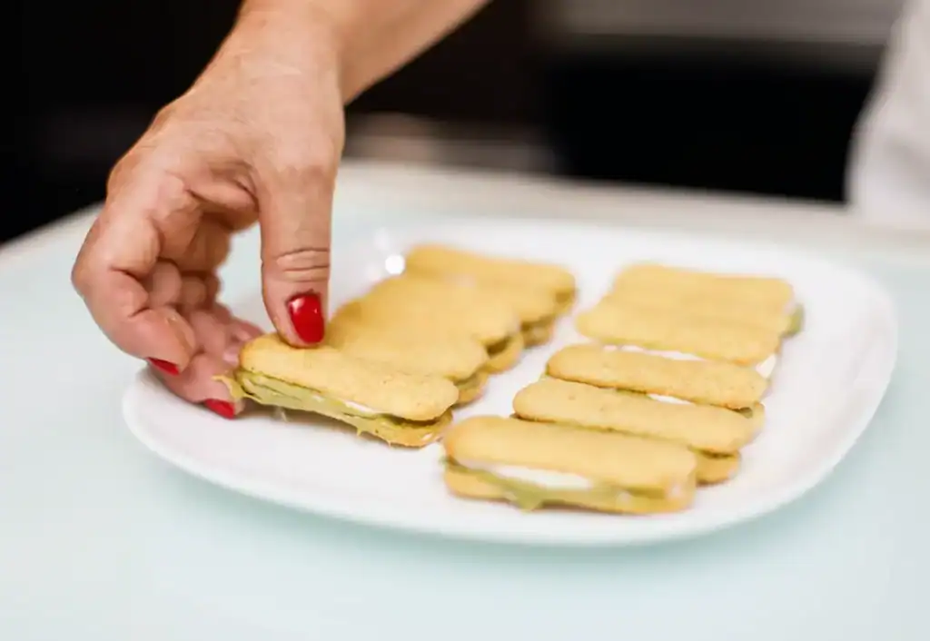 Delicious Sicilian Cannoli Cookies Hand holding a cannoli cookie with cream filling on a white plate.