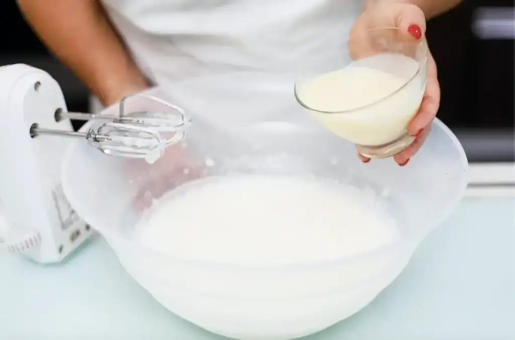 Farcitura di crema in ciotola e fruste Person holding a bowl of creamy filling over a large mixing bowl with beaters.