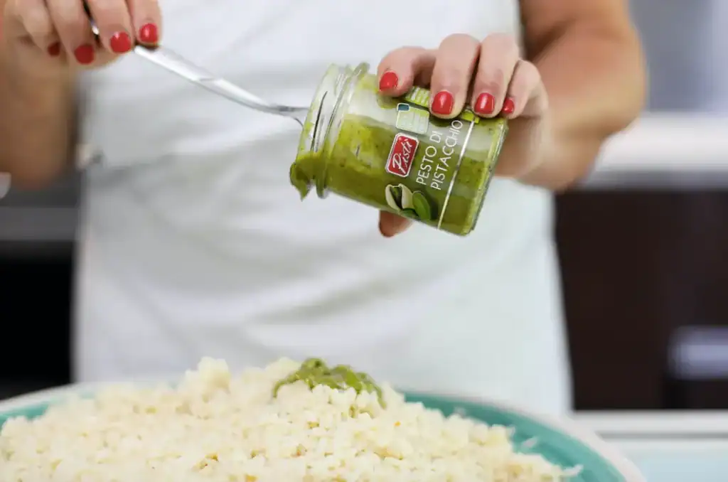 Pomodoro Verde Pistì – Salsa Artigianale Siciliana Person adding Sicilian green pistachio sauce to rice dish.