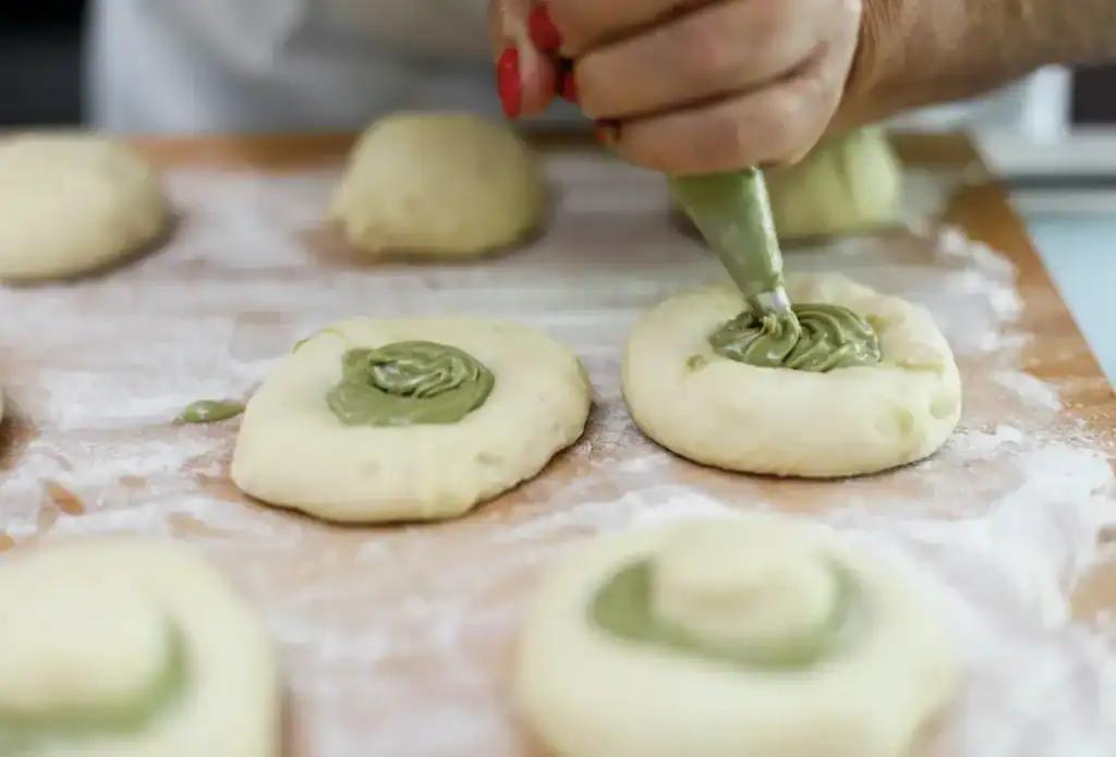 Pistì artisanal Sicilian sweets preparation Hand piping green pistachio filling onto dough circles for Sicilian sweets.