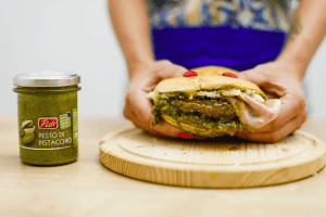 Pistachio pesto in jar with a person holding a pistachio-filled pastry.