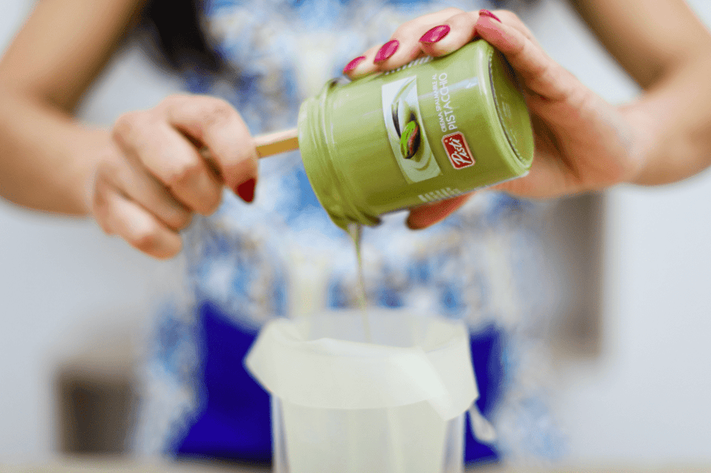 Creamy Pistachio Spread Woman pouring pistachio spread from jar into paper bag, close-up.