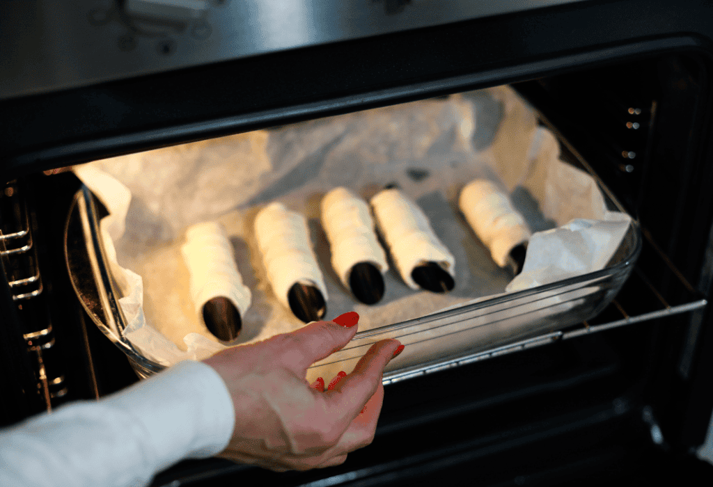 Fagottini di cioccolato in forno Hand placing chocolate-filled pastry rolls in oven for baking.