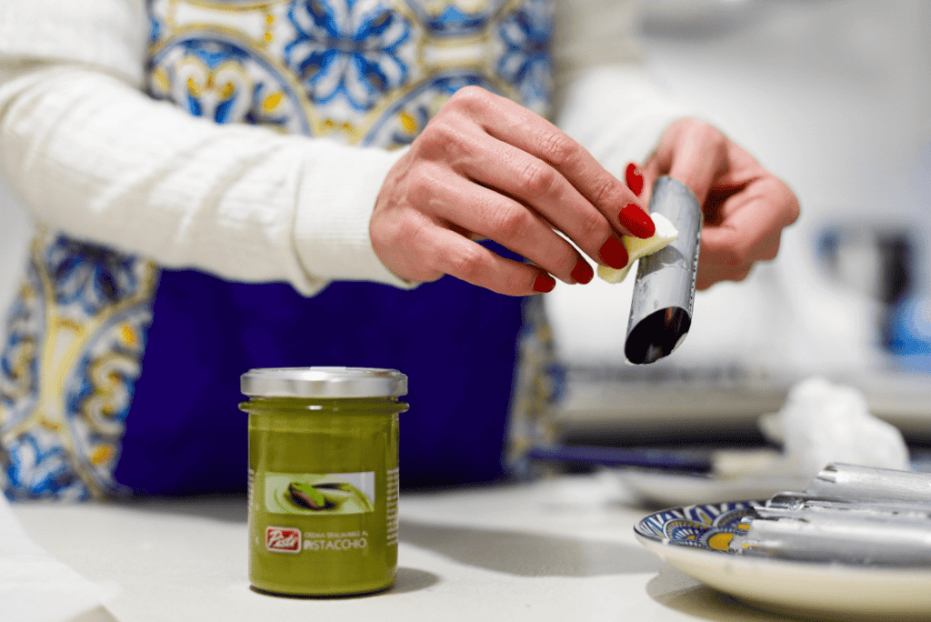 Pistì Sicilian Artisanal Pistachio Spread Woman preparing Sicilian pistachio spread with a jar of pistachio paste.