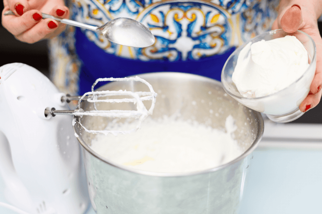Crema di ricotta fresca Donna che versa crema di ricotta in una ciotola con frusta elettrica.
