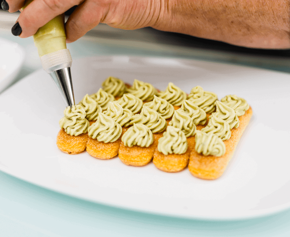 Tartelle con crema di pistacchio Artisanal pistachio cream tartlets being decorated with a piping bag.