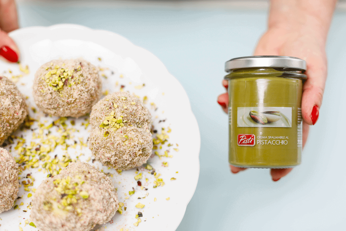 Hand holding pistachio cream jar with Sicilian sweets on a plate.