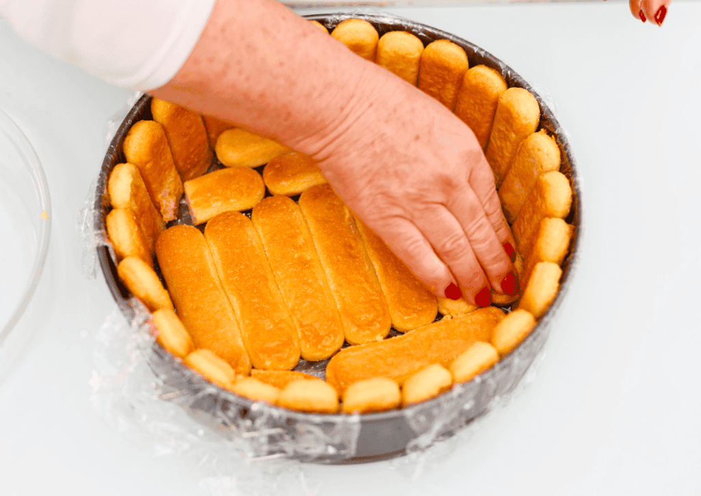 Torta di biscotti e crema Preparazione di una torta di biscotti e crema con mani che sistemano i biscotti in una teglia.