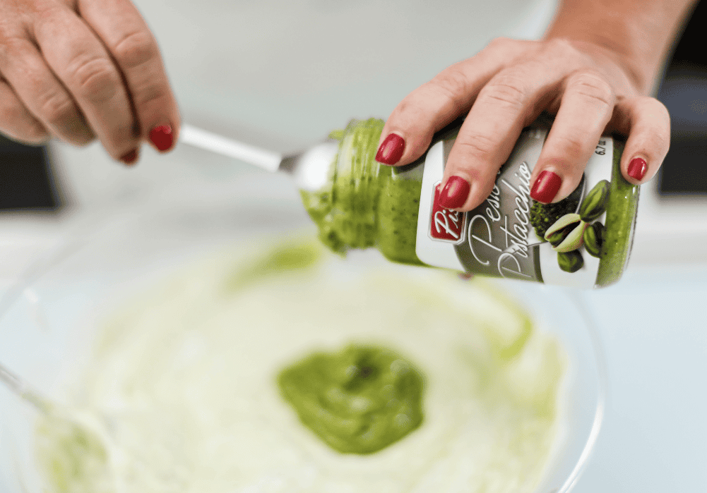Pomodoro Verde Artisanal Sauce Hand pouring green pesto sauce into a bowl, close-up of hands with red nails.