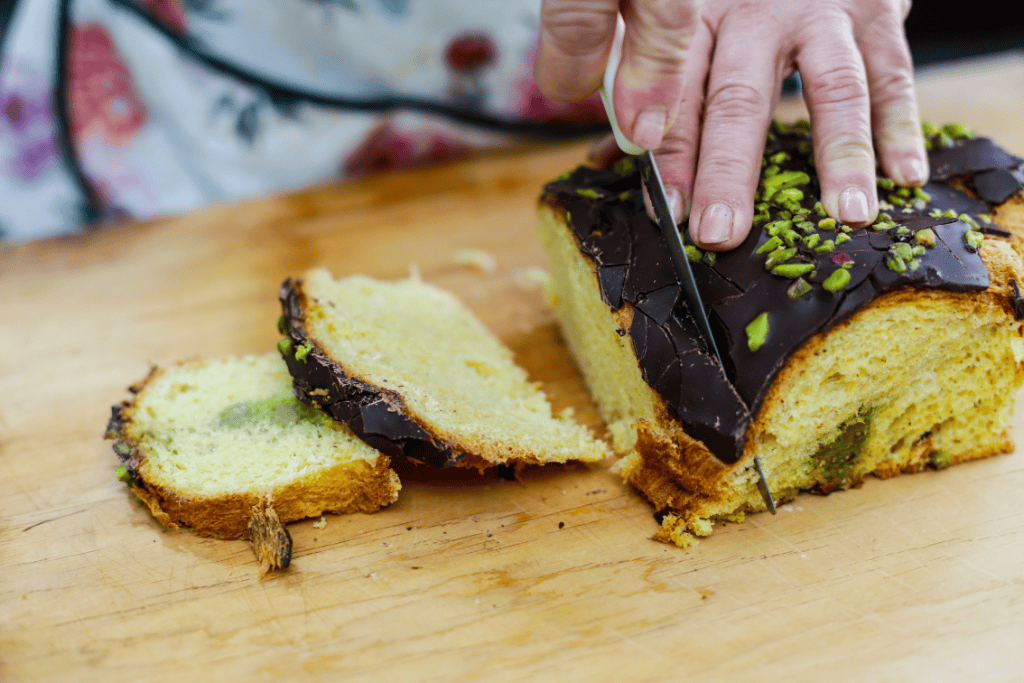 Sweet Lemon Cake Slice of lemon cake with chocolate glaze and pistachio topping on wooden board.