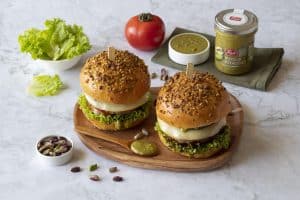 Two artisanal Sicilian-style burgers with fresh lettuce, cheese, and crunchy topping on a wooden pla.