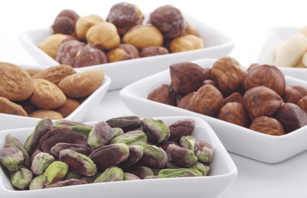Assorted Sicilian nuts including hazelnuts, pistachios, and almonds in white bowls.