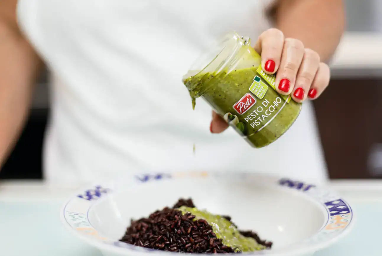 Woman pouring green pistachio pesto onto rice dish.
